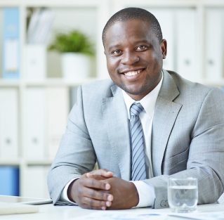 Image of happy young businessman looking at camera at workplace